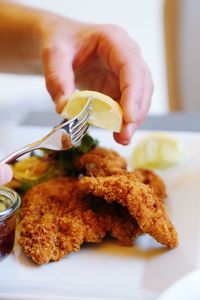 Close-up of hand holding and pressing lemon juice on top of the wiener schnitzel 