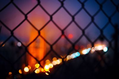 Close-up of illuminated chainlink fence against sky at night