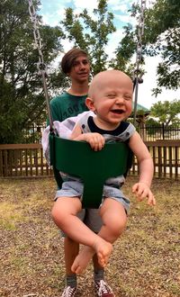 Teenage boy standing by cute brother swinging in playground