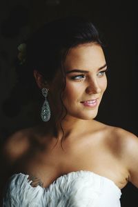 Close-up of beautiful smiling woman wearing gown looking away against black background