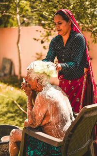 Daughter bathing her old mother in yard