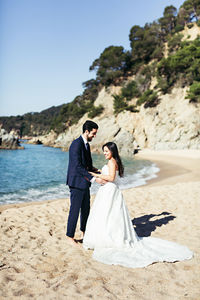 Newlywed couple enjoying at beach against clear sky during sunny day