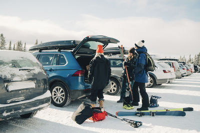 Female and male friends loading skis in trunk car during winter