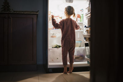 Rear view of girl standing by refrigerator at home