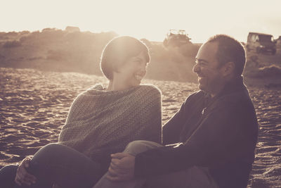 Happy couple sitting at beach during sunset