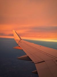 Cropped image of airplane flying over clouds during sunset