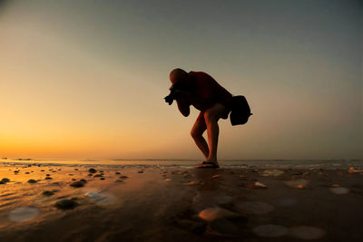 Side view of woman standing on beach against sky during sunset