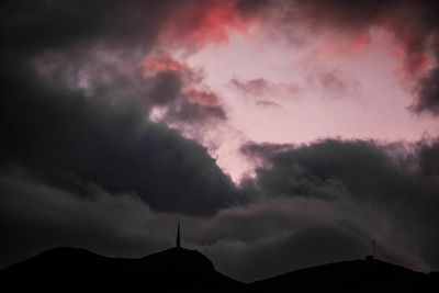 Low angle view of storm clouds over silhouette mountain