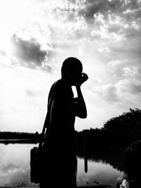 Silhouette man photographing lake against sky