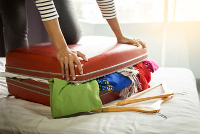 Midsection of woman closing suitcase on bed