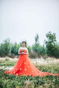 Woman in wedding dress on field against sky