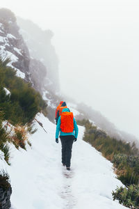 Rear view of man on mountain against sky during winter