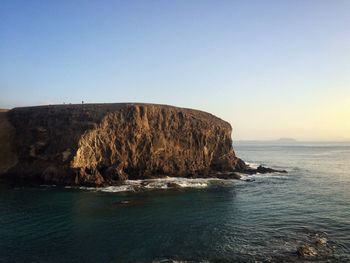 Rock formations in sea against clear blue sky