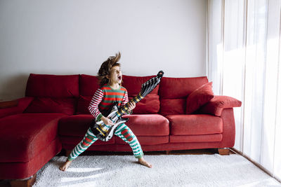 Happy girl playing guitar against sofa in living room