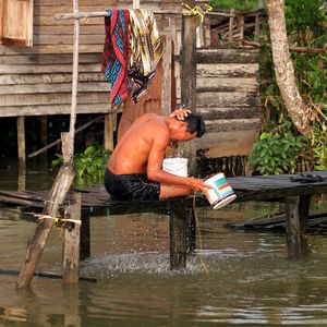 Man bathing while sitting on pier over lake