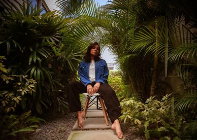 Full length of young woman sitting on palm tree