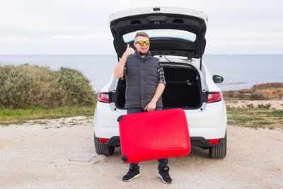 Portrait of man standing on car against sky