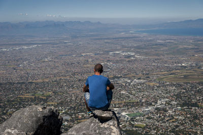 Rear view of man sitting in city against sky