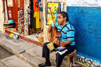 Full length of boy sitting by graffiti on wall