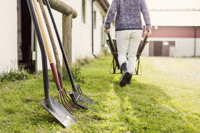 Work tools arranged by barn while woman pushing wheelbarrow at farm