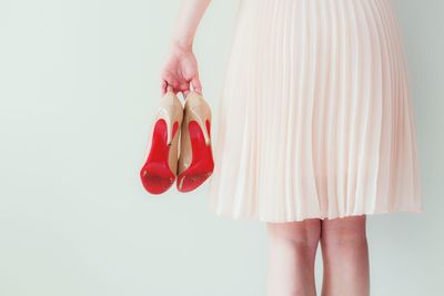 Rear view of woman holding high heels against wall