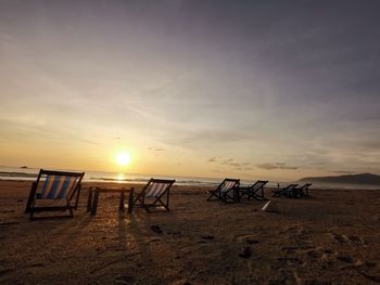 Deck chairs on beach against sky during sunset