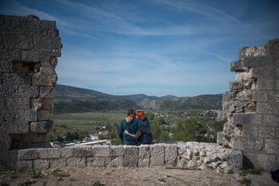 Couple kissing while sitting on retaining wall against sky