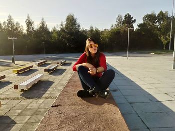 Young woman sitting on tree against sky