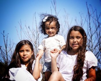Happy friends sitting on bare tree against sky