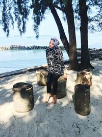 Young woman sitting on tree stump at beach