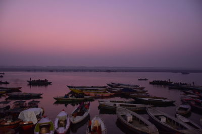 Boats moored in harbor at sunset