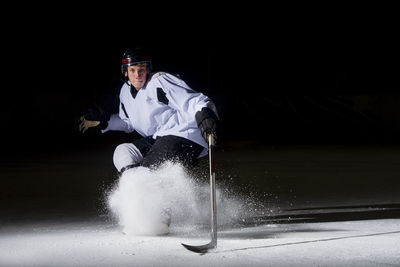 Portrait of man playing ice hockey against black background