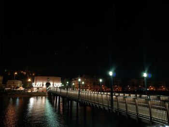 Illuminated bridge over river against sky at night