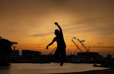 Silhouette man with arms raised against sky during sunset
