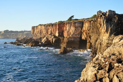 Rock formations by sea against clear sky