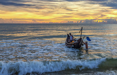 Man in boat on sea against sky during sunset