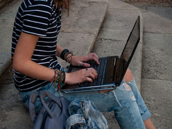 Midsection of woman using laptop while sitting on staircase