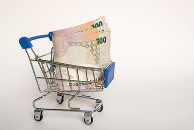 Close-up of paper currency in shopping cart against white background