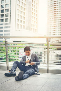 Businessman looking at wallet while sitting on elevated walkway