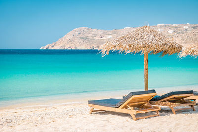 Deck chairs on beach against blue sky, mykonos greece 