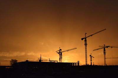 Silhouette cranes at construction site against sky during sunset