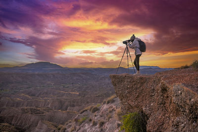 Rear view of man standing on mountain against sky during sunset