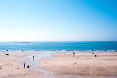 People on beach against clear blue sky