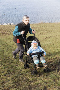 High angle view of grandfather pushing granddaughter sitting in baby stroller on grassy field