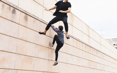 Low angle of anonymous men athlete in sports outfit jumping on wall and pushing off it during training near building