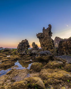 Rock formation on shore against sky during sunset