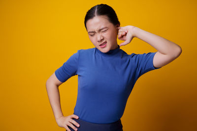 Young woman looking away while standing against yellow background