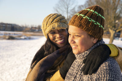 Smiling mature woman standing with arm around looking at son wearing knit hat