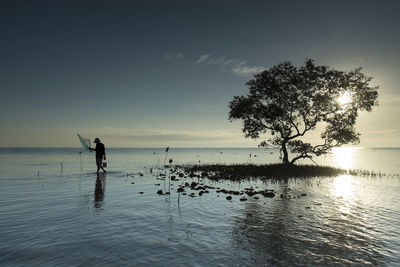 Silhouette man walking in sea against sky during sunset