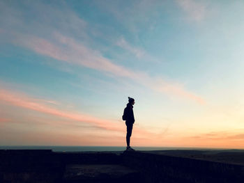 Silhouette man standing on street against sky during sunset